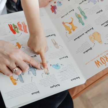 A child and adult engaging with an educational book, pointing to illustrations.