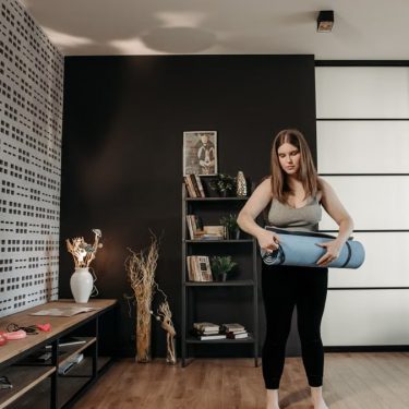Plus size woman rolling a yoga mat in a stylish indoor setting with modern decor.